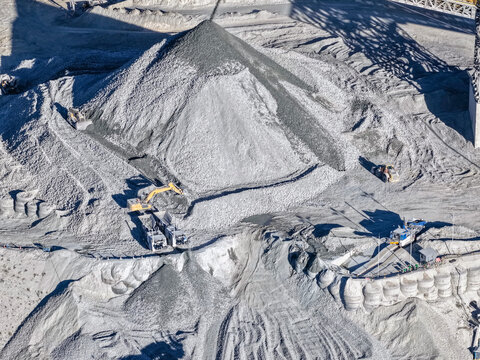 Huge pile of gray aggregate with a hydraulic excavator at a mining plant, aerial view