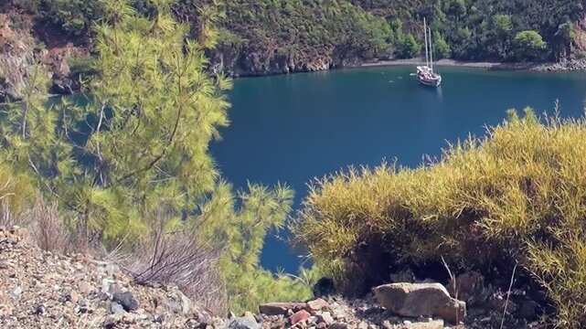 A breathtaking view unfolds over Oludeniz Bay Turkey, revealing its deep blue waters. A serene sailboat gently rests in the secluded cove, framed by rugged green hills and a bright sunny sky.