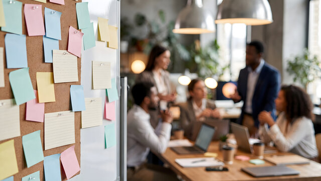 Sticky Notes on Office Board with Diverse Team Brainstorming in Blurred Background