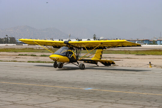 Yellow ultralight aircraft parked on the runway with hills and clear sky in the background