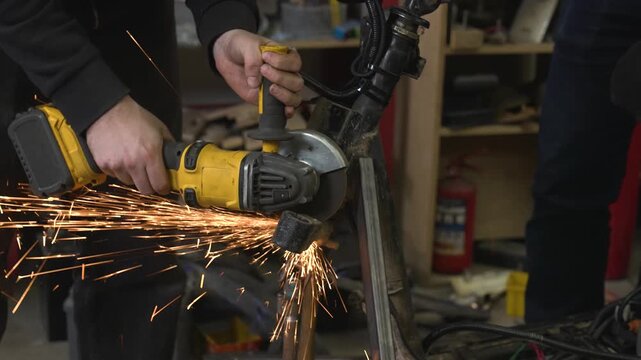 A worker uses a grinder to cut off excess parts from a snowmobile's metal frame, sparks flying in all directions.
