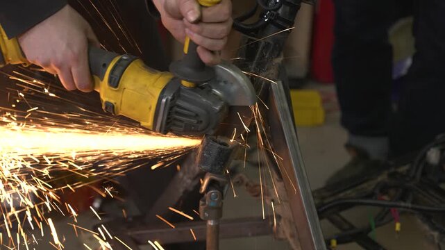 A worker uses a grinder to cut off excess parts from a snowmobile's metal frame, sparks flying in all directions.