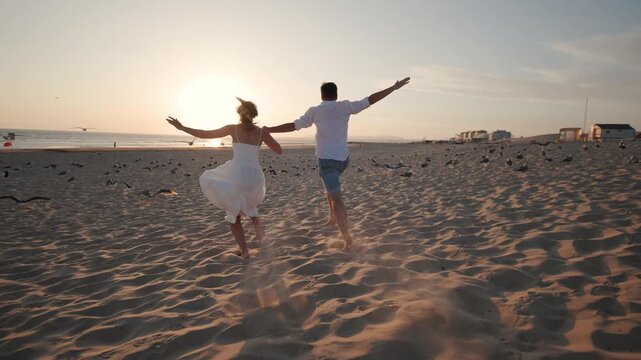 Couple runs on the beach at sunset in a warm and lively moment of joy