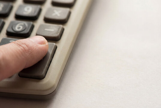 A close-up shot of a person's finger pressing the equals button on a beige calculator, indicating calculation or financial work.