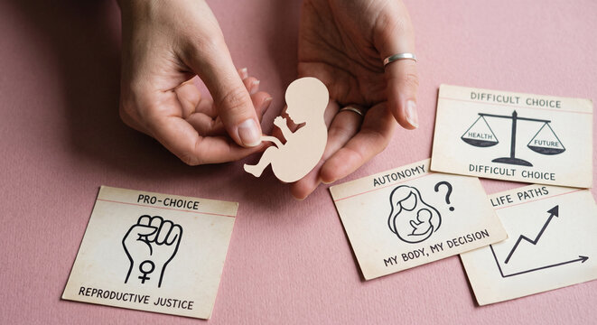 Hands holding a paper cutout of a fetus surrounded by pro-choice and reproductive justice cards on a pink background illustrating reproductive rights discussion