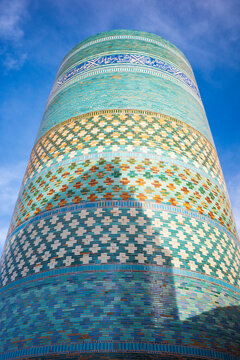 Low-angle close-up of the iconic Kalta Minor Minaret in Khiva, Uzbekistan, showcasing vibrant turquoise glazed tiles, intricate geometric patterns, and elegant Arabic calligraphy