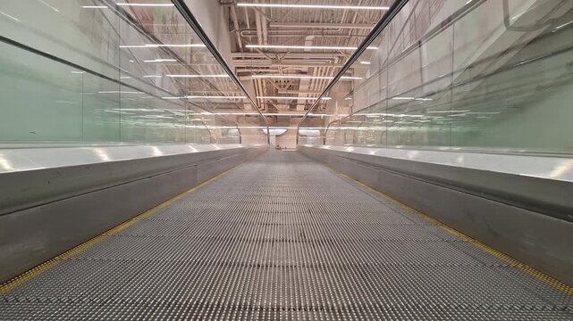 An empty moving walkway stretches forward inside a modern spacious public building, transport infrastructure, urban architecture.
