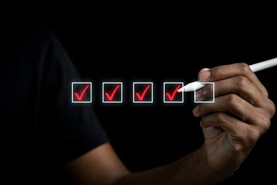 Hand using a digital stylus pen to check off boxes on a virtual checklist against black background