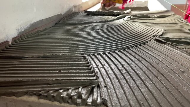 Wet cement adhesive spreads on the floor with notch trowel for tile installation.
