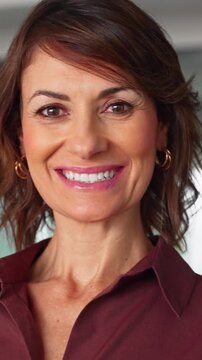 Close up portrait of happy latin businesswoman looking at camera in office. Smiling mature woman, beautiful face with toothy smile. Cheerful female business executive enjoys career at work. Vertical