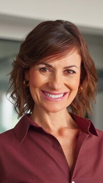 Close up face portrait of middle aged mature businesswoman in office. Attractive woman looks at camera with light smile. Female business director, professional in 50s poses at workplace. Vertical