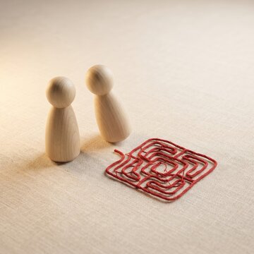 Two Wooden Figures Facing a Tangled Thread Maze Together