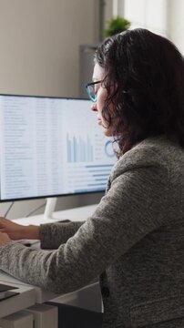 Woman analyst accountant at office computer analyzing spreadsheet. She checks figures on multiple monitors for accuracy and timely corporate reporting. Clear concept of financial data analysis.