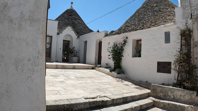 Alberobello, Puglia, Italy. Upward camera reveal of traditional whitewashed trulli houses, conical stone roofs and a sunlit courtyard in the UNESCO-listed historic town.