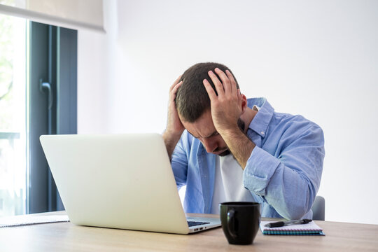 Man covering his head with hands, feeling intense frustration and burnout while working on a laptop, depicting stress, workload, and pressure in a modern office or home office setting