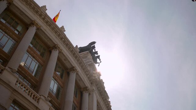 Low-angle rooftop silhouette, neoclassical building corner with tall columns, ornate entablature, balustrade, multi-pane windows, sunbacklit statuary, flag, with architecture, building, column