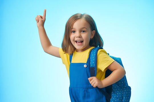 Excited young schoolgirl with a backpack pointing up towards something interesting against a blue studio background