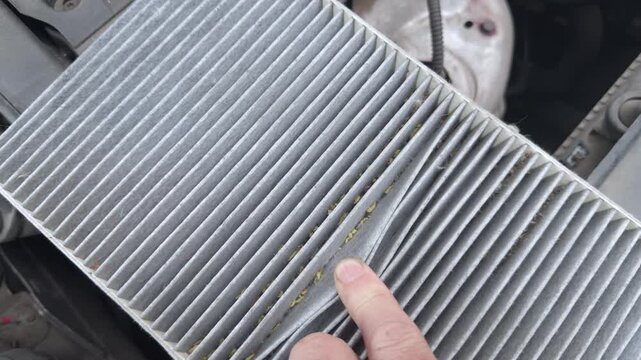 A finger points to debris between the pleats of a dirty cabin filter
