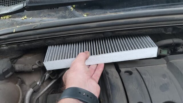 A hand removes a dirty cabin filter from a car compartment