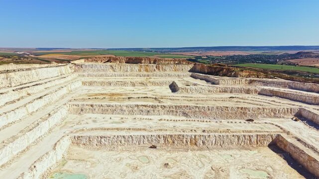 Workers are present at the quarry site focusing on tasks such as excavation and transportation of materials. The landscape shows distinct layers of rock and earth.