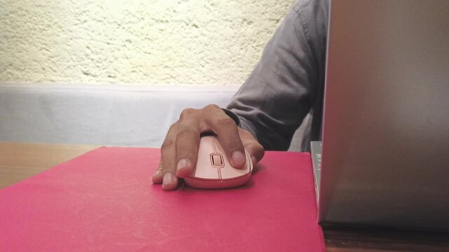Front view close up of person hand holding and clicking pink wireless computer mouse on red desk pad