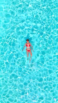 Top down view of a woman in pink swimsuit swims on her back in the pool.