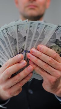Formally dressed man is counting US Dollar bills, close-up.