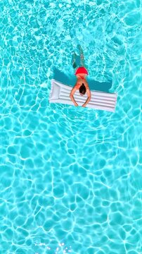 Aerial view of a woman in red swimsuit swimming in the pool. Summer lifestyle