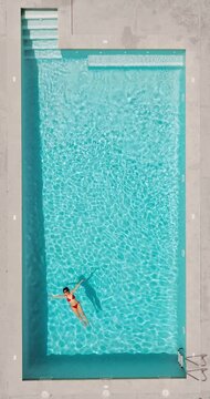 Top down view of a woman in redre swimsuit lying on her back in the pool.