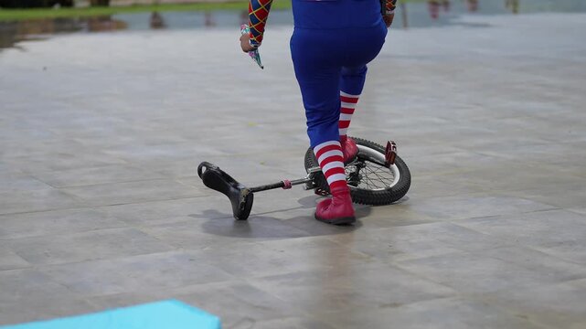 Clown trying to get on a unicycle incorrectly

