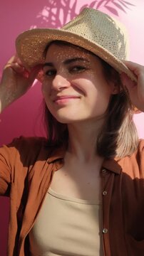 Vertical video of young beautiful happy brunette woman in straw hat smiling on the pink background