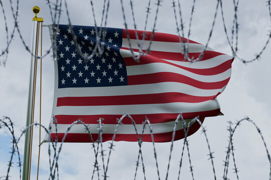 American flag waving on a flagpole, viewed through sharp coiled barbed wire against a cloudy sky. Conceptual image representing US immigration policy, border security, and illegal migration control.