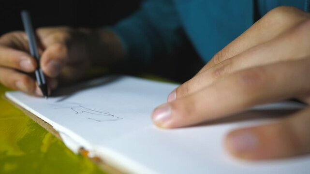 Male hand holds a ball pen and draws black lines in sketchbook. Close up of arm of talented artist paints beautiful abstract image on white paper. Artistic and creativity concept. Slow motion