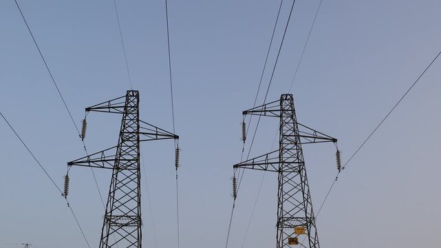 Low angle shot of two high voltage power pylons and electrical cables against a clear sky.