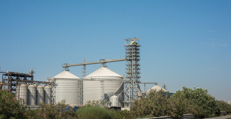 Grain storage silos and processing facility illuminated by sunrise featuring connected industrial buildings and towering elevator structures within the agricultural landscape of California © ChristopherTP