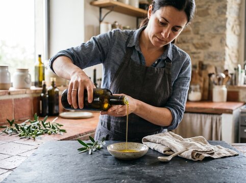 Woman pouring fresh extra virgin olive oil into a small ceramic bowl in a rustic kitchen setting