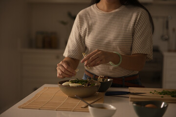 African American woman preparing ceramic bowl of noodles on bamboo mat at counter with scallions © wavebreak3