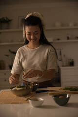 Adult Asian woman preparing meal in home kitchen, adding chopped herbs on wooden cutting board © wavebreak3