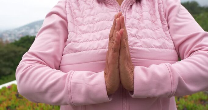 African American senior pressing palms adjusting fingers starting namaste in pink jacket on terrace