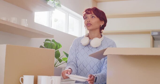 African American woman unpacking boxes at counter taking white plates checking gap placing on shelf