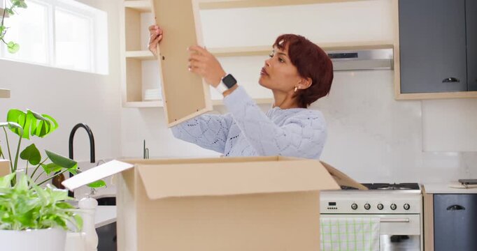 African American woman reaching into box lifting framed print planning wall spot in kitchen