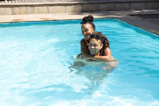African American couple laughing and splashing in shallow backyard pool with sunglasses, copy space
