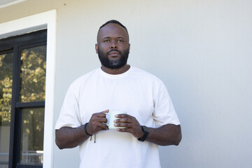 Mid-adult African American man standing at sliding glass door holding white mug and wearing watch © wavebreak3