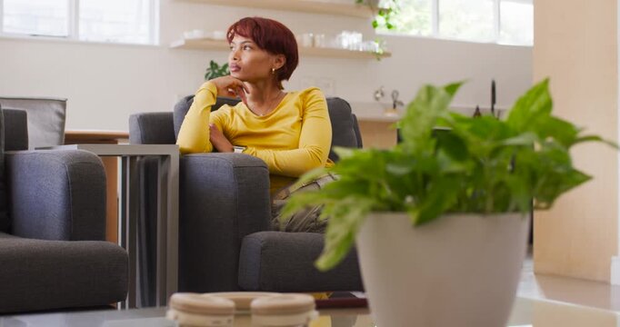 African American woman sitting in gray chair, tracking motion outside bright window and reflecting
