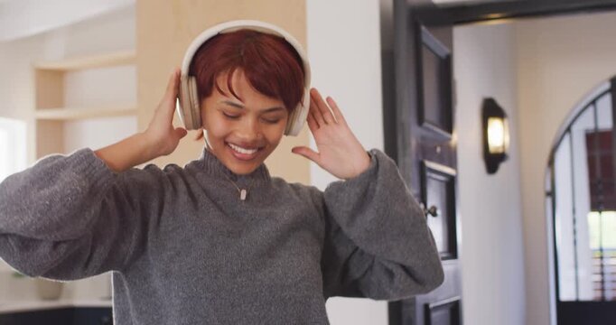 Woman in gray sweater with white headset hearing music singing adjusting fit and dancing in kitchen