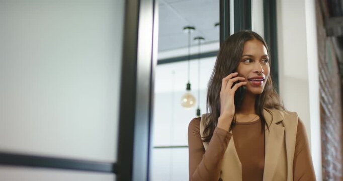 African American woman 20s in vest receiving call with smartphone in office laughing, copy space