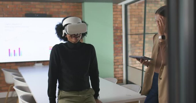 African American pair demoing VR headset in office, woman using tablet, man in turtleneck reacting