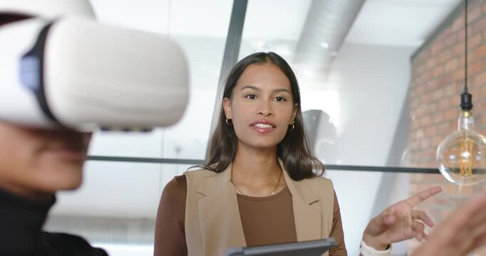 Female team demoing at office lead in blazer holding tablet guiding VR user wearing white headset