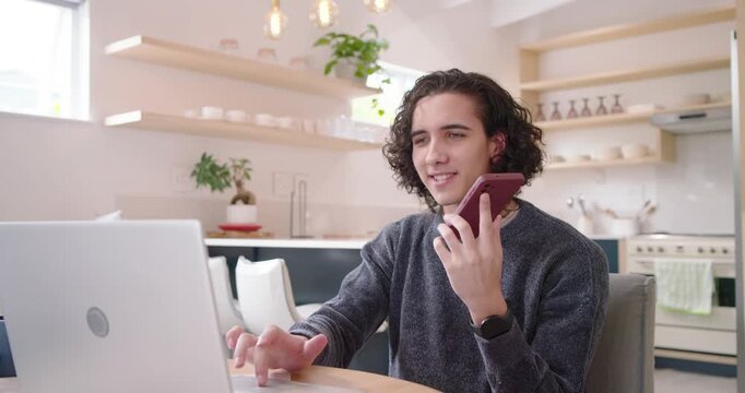 African American man early-20s receiving work call, holding smartphone typing on laptop in kitchen