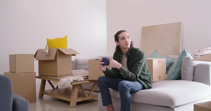 African American man sitting on light sectional sofa in apartment during move-in, sipping blue mug